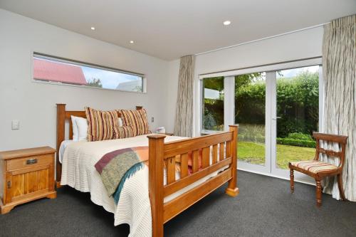 a bedroom with a bed and a chair and windows at Jeffreys Road - Christchurch Holiday Homes in Christchurch