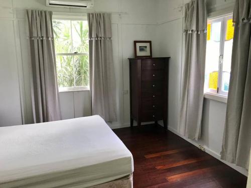 a bedroom with a bed and a dresser and two windows at Original Surf Cottage in heart of Pottsville Beach in Pottsville