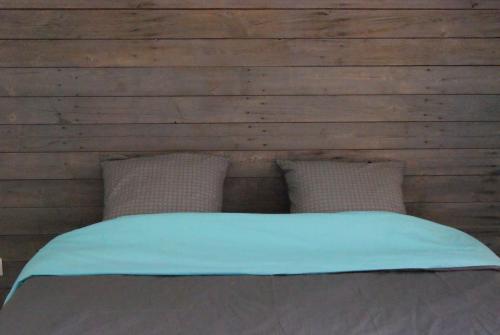 ein Bett mit zwei Kissen vor einer Holzwand in der Unterkunft GrIsa'Home in Aisonville-et-Bernoville
