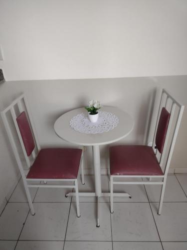 uma mesa branca com duas cadeiras e um vaso de flores em Studio no Centro em Araxá