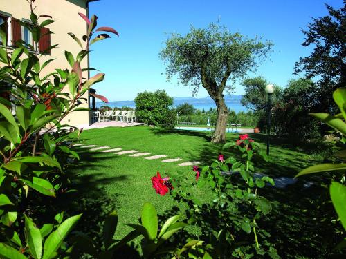 a green yard with a tree and red flowers at Agriturismo Il Giardino Degli Ulivi in Lazise