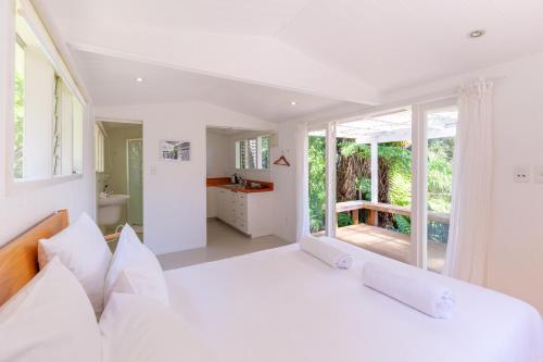 a white bedroom with a large bed and large windows at Koi Waiheke with private beach access and mooring in Omiha