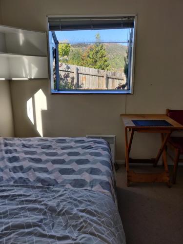 a bedroom with a bed and a window with a table at wanaka plantation road room in Wanaka