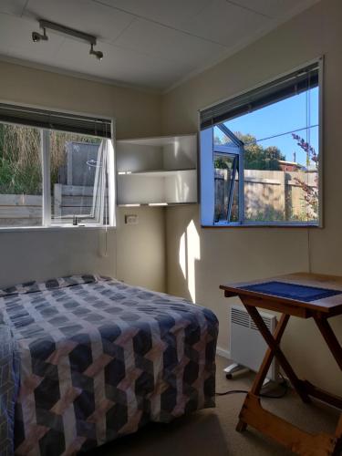 a bedroom with a bed and a table and two windows at wanaka plantation road room in Wanaka