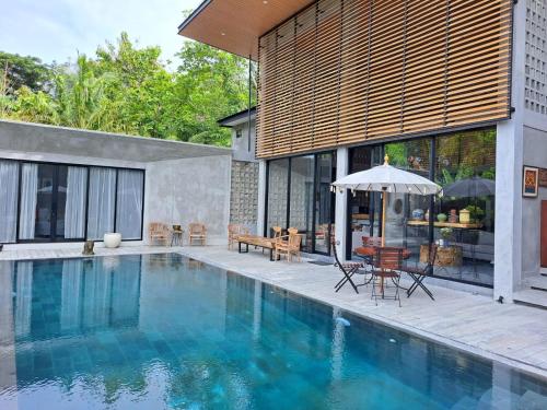a house with a swimming pool with a table and an umbrella at DJipangan Home in Bantul