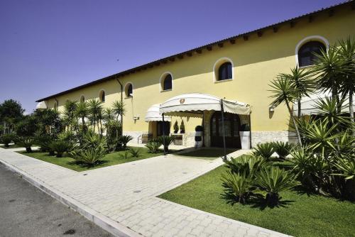 a yellow building with a white awning and palm trees at Hotel Tenuta San Francesco in Barletta