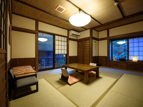 a room with a table and a bench and windows at Yunohira Kamiyanagiya in Yufuin