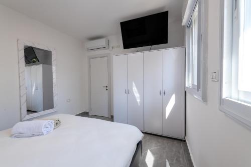 a white bedroom with a bed and a flat screen tv at Kings suite at Royal Park Eilat in Eilat