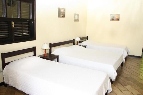 three beds in a room with white sheets at Pousada Ribeirão do Ouro in Itamonte