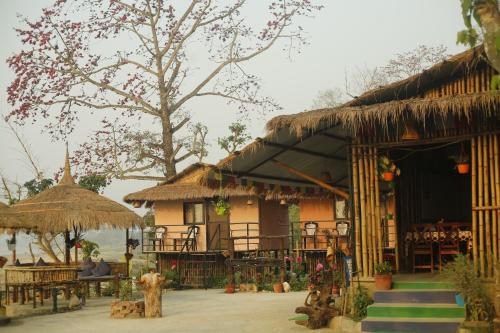una casa con techo de paja, mesas y sillas en Bamby Chilling House - Feel The Nature en Sauraha