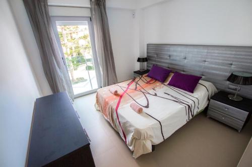 ein Schlafzimmer mit einem Bett mit lila Kissen und einem Fenster in der Unterkunft Moderno y bonito apartamento en primera linea de playa de poniente in Benidorm