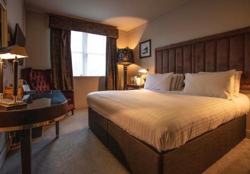 a bedroom with a large bed with a desk and a window at Strathaven Hotel in Strathaven