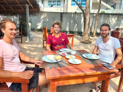 three men sitting at a wooden table with food on it at Hotel Coral Bay in Trincomalee