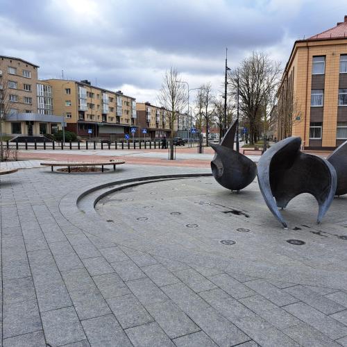 a sculpture in a park with a bench and buildings at Sweet home in Šiauliai