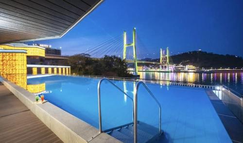 Yeosu Hotel Haven في يوسو: مسبح في الليل مع وجود جسر في الخلفية