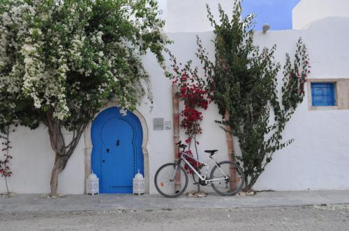 un vélo garé devant un bâtiment blanc avec une porte bleue dans l'établissement Dar Bibine, à Erriadh