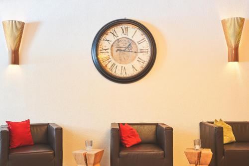 a clock hanging on a wall above two chairs at Hotel Fischer am See in Heiterwang
