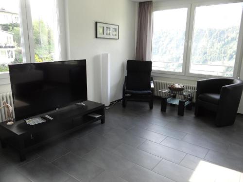 a living room with a flat screen tv and two chairs at Apartment Barbara Ost by Interhome in Engelberg