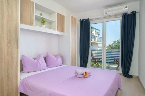 ein Schlafzimmer mit einem Bett mit lila Kissen und einem Fenster in der Unterkunft Apartmani Gabriella in Vodice
