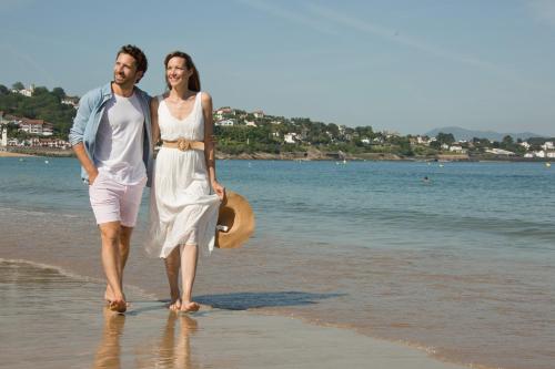 a man and a woman walking on the beach at Grand Hôtel Thalasso & Spa in Saint-Jean-de-Luz