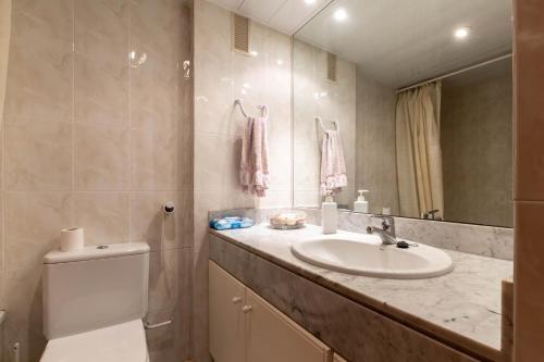 een badkamer met een wastafel, een toilet en een spiegel bij AT053 Els Pins, primera línea con piscina, airco in Torredembarra
