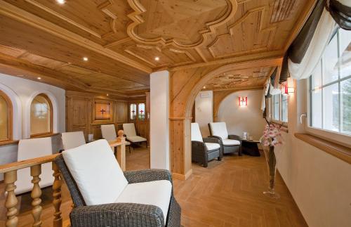 a living room with a wooden ceiling and chairs at Hotel Des Alpes in Soraga