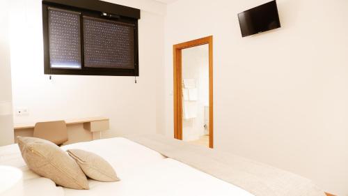a white bedroom with a bed and a television at Hotel Ocamiño in Durango