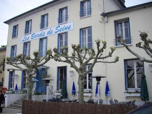 um edifício branco com árvores em frente em LOGIS Hôtel & Restaurant - Les Bords de Seine em La Roche-Guyon