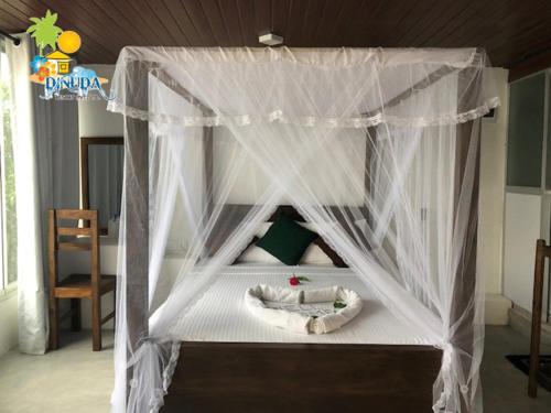 a canopy bed with white drapes in a bedroom at Dinuda Resort in Kalpitiya