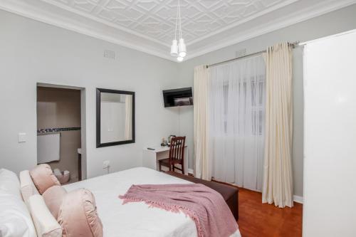 a white bedroom with a bed and a chair at Paradise Guest House in Roodepoort