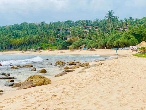 ein Strand mit Felsen im Wasser und ein Resort in der Unterkunft Sanderling Silent Beach Cabanas in Tangalle