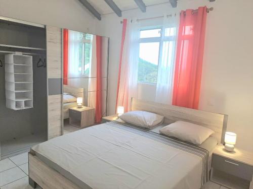 a bedroom with a bed and a window with red curtains at La Familiale in Sainte-Rose