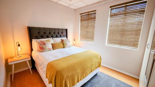 a bedroom with a bed with a yellow blanket and a window at The Skinny Expat in Paarl