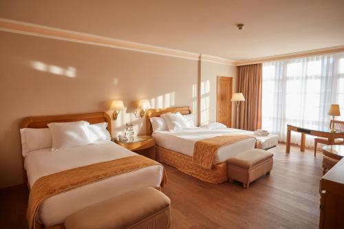 a hotel room with two beds and a desk at Gran Hotel Los Abetos in Santiago de Compostela