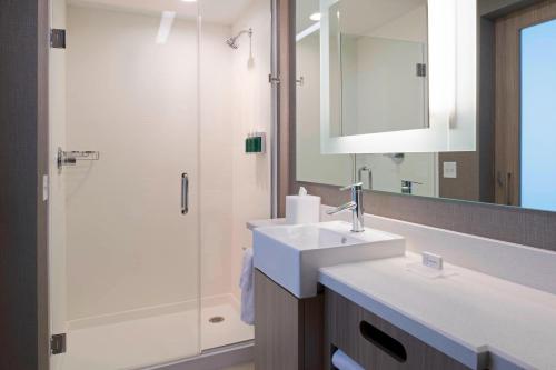 uma casa de banho com um lavatório e um chuveiro com um espelho. em SpringHill Suites by Marriott East Lansing University Area, Lansing Area em East Lansing
