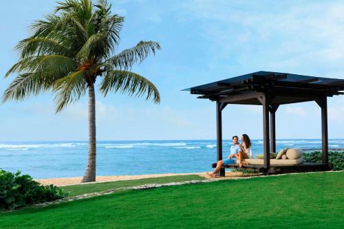 two people sitting on a bench next to the ocean at The Ritz-Carlton Bali in Nusa Dua