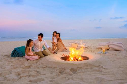 a group of people sitting around a fire on the beach at The Ritz-Carlton Bali in Nusa Dua