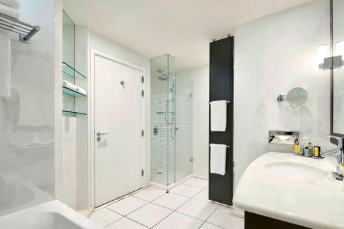 ein weißes Bad mit einer Dusche und einem Waschbecken in der Unterkunft Lyon Marriott Hotel Cité Internationale in Lyon