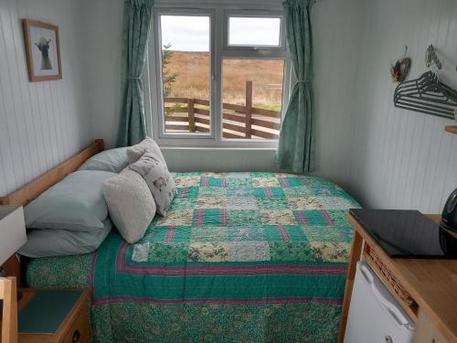 a bedroom with a bed with a quilt and a window at Hillside Camping Pods and Shepherd's Hut in Wick