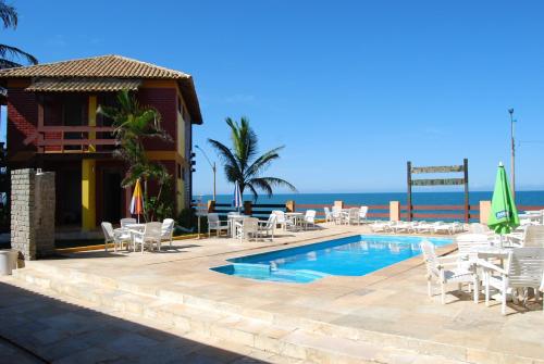 um resort com piscina e cadeiras e o oceano em Pousada Portal da Barra em Marataízes