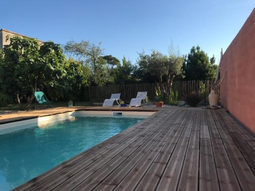 a swimming pool with a wooden deck and two chairs at Villa des Oliviers in Baillargues
