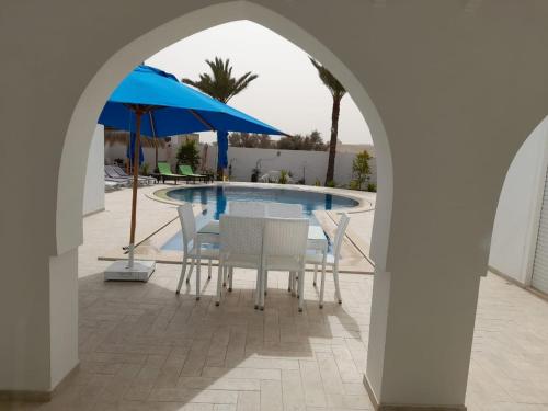 una mesa y sillas bajo una sombrilla junto a la piscina en Villa La Palmeraie d'Arkou, grande piscine en Arkou