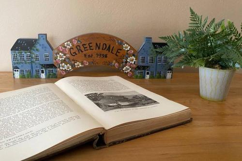 een open boek op een tafel met huizen en een plant bij A Showplace of Greendale History on Apple Court in Greendale