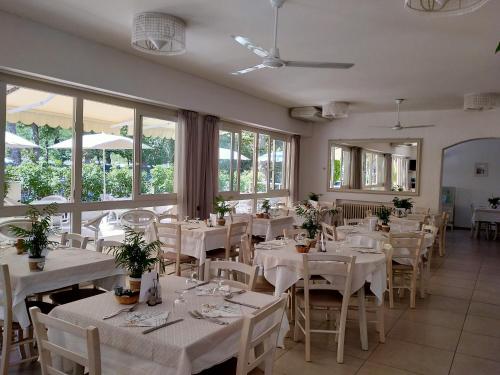 un restaurante con mesas y sillas blancas y ventanas en B&b villa lambusta en Cesenatico