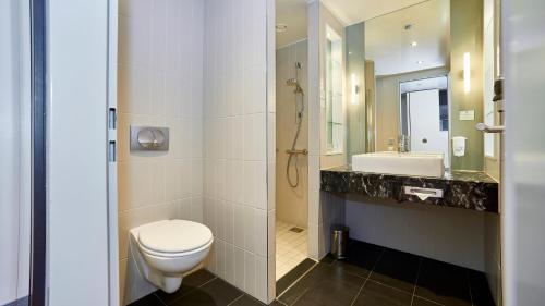 a bathroom with a toilet and a sink and a mirror at Holiday Inn Berlin Airport - Conference Centre by IHG in Schönefeld
