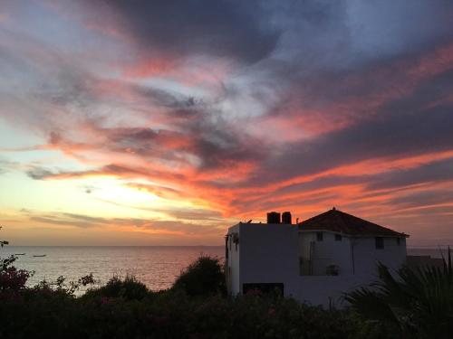a sunset with a white building in front of the ocean at Résidence Keur Fleurie in Toubab Dialaw