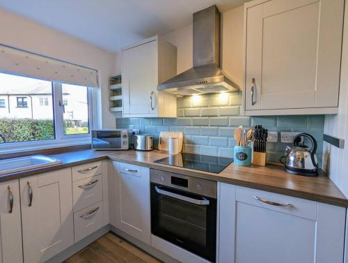 een keuken met witte kasten en een fornuis met oven bij Parkview Cottage - Lovely home overlooking park in Carnoustie