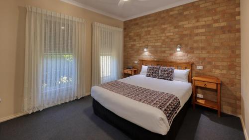 1 dormitorio con 1 cama grande y pared de ladrillo en Bridges on Meninya Motel & Apartments, en Moama