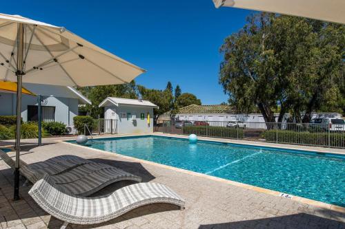a swimming pool with two lounge chairs and an umbrella at Escape to 64 at Cape View Resort in Busselton