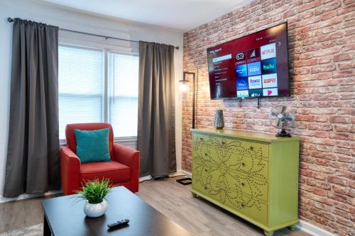 uma sala de estar com uma cadeira vermelha e uma televisão numa parede de tijolos em Trendy Escape ◉ California King bed awaits! em Charlotte